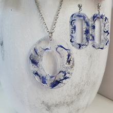 Load image into Gallery viewer, Handmade real flower oval pendant necklace accompanied by a pair of stud dangling earrings made with blue cornflower and silver flakes preserved in resin. Resin Flower Jewelry - Necklace And Earring Set